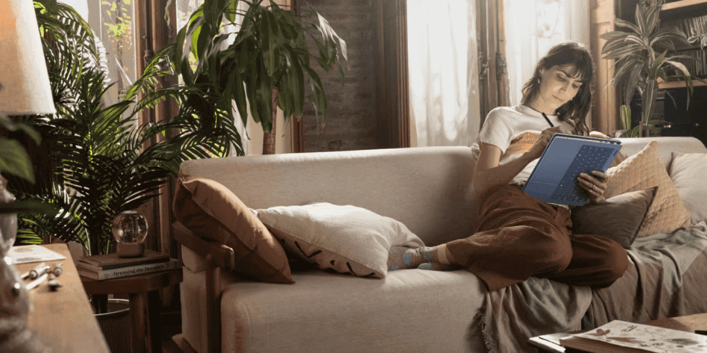 A woman is looking at her HP OmniBook X Flip 14 while relaxing on a beige couch in a cozy, plant-filled living room with natural lighting and bookshelves in the background. Share HP OmniBook X Flip 14: Is It the Best Convertible Laptop for Modern Professi