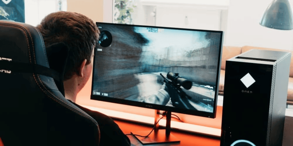 A gamer wearing headphones playing a first-person shooter game on a monitor next to an OMEN gaming PC tower with LED lighting.